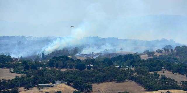 A plane flies over smoke from fires burring across the Adelaide Hills, near Adelaide, Australia, Saturday, Jan. 3, 2015. Thousands of Australians fled their homes as wildfires raged across the nation's south on Saturday, with firefighters struggling to contain the blazes as strong winds fanned the flames. (AAP IMAGE/ DAVID MARIUZ) EDITORIAL USE ONLY, AUSTRALIA OUT, NEW ZEALAND OUT, PAPUA NEW GUINEA OUT, SOUTH PACIFIC OUT, NO ARCHIVES