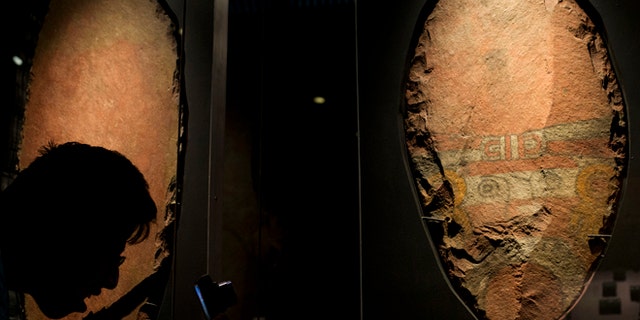A man bends down to take a picture of a giant, symbolic sacrificial knife, part of a display of items offered to the Aztec god Xochipilli, at the Templo Mayor museum in Mexico City, Friday, Aug. 7, 2015. The Aztecs usually sacrificed quails to Xochipilli, rather than still-beating human hearts. And he was worshipped at vast poetry and music festivals, rather than martial displays. (AP Photo/Rebecca Blackwell)