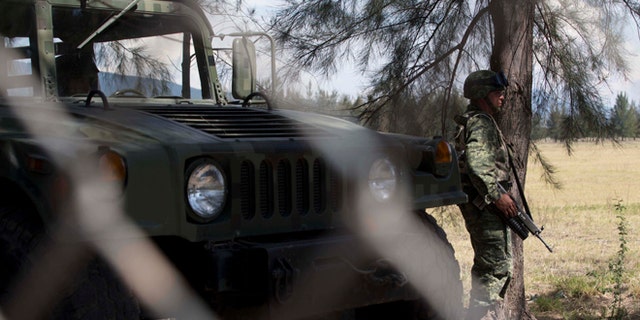 A Mexican Army soldier, seen through a chain-linked fence, stands guard near the entrance of Rancho del Sol, near Vista Hermosa, Mexico, Friday, May 22, 2015. (AP Photo/Refugio Ruiz)