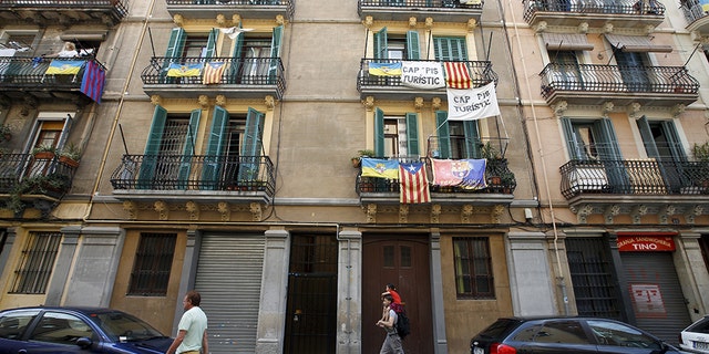 Banners against touristic apartments hang from balconies as people walk past them at Barceloneta neighborhood in Barcelona, Spain. The banner reads "no touristic apartments."