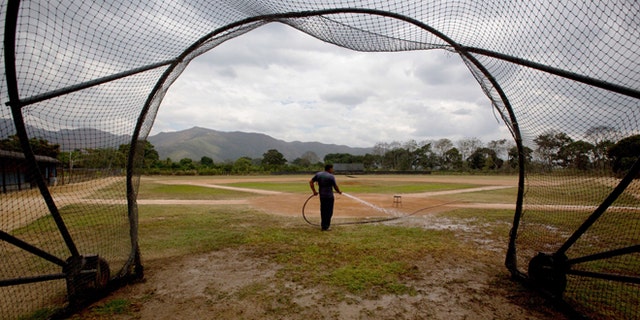 In this March 10, 2015 photo, Seattle Mariners ground worker Carlos Galindez sprays water on the field after a training session at the Seattle Mariners' baseball academy in Aguirre, Venezuela. The teamâs operations are coming to an abrupt end and moving to Dominican Republic, the latest in a string of American teams that have abandoned Venezuela in the past decade as a result of economic turmoil, rampant crime and mounting tensions with the United States. âI donât know why theyâre going,â said Galindez, holding back tears as he reflected proudly on his work caring for the academyâs two baseball diamonds. âAll I can say is they treated us well.â (AP Photo/Fernando Llano)