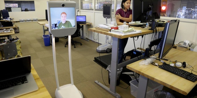 Dec. 12, 2012: Senior software engineer, Josh Faust, seen on screen, navigates his company's office using a Beam remote presence system, as fellow engineer Stephanie Lee, at right, works on a project at Suitable Technologies in Palo Alto, Calif.