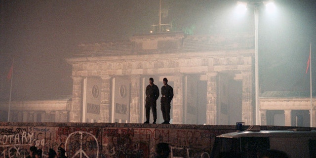 In this November 1989 file photo, two East German border guards patrolled atop the Berlin Wall with the illuminated Brandenburg Gate in the background.