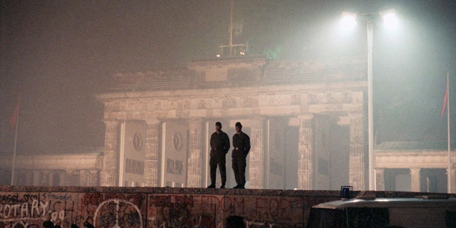 In this November 1989 file photo, two East German border guards patrolled atop the Berlin Wall with the illuminated Brandenburg Gate in the background.