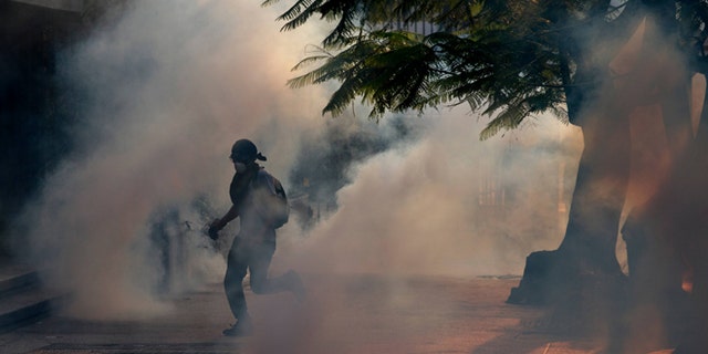 A demonstrator take cover from tear gas fired by Bolivarian National police during clashes with anti-government protesters in Caracas,Venezuela, Saturday, March 8, 2014. The Venezuelan government and opposition appear to have reached a stalemate, in which street protests continue almost daily while the opposition sits out a peace process it calls farcical. (AP Photo/Fernando Llano)
