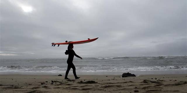 This file photo shows a surfer carrying her surfboard in Half Moon Bay, Calif.
