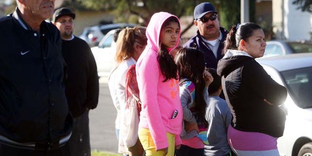 Neighbors look on as police investigate house where a family of four were found shot to death.