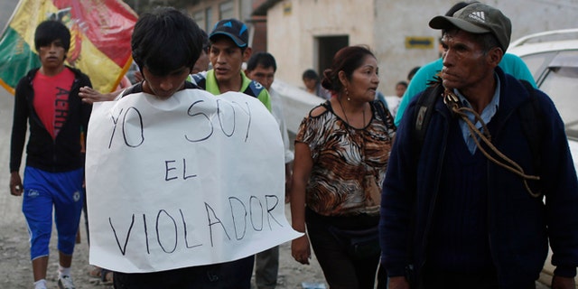 In this June 6, 2015 photo, a man is made to wear a sign with a handwritten message that reads in Spanish; "I'm the rapist," as he is paraded through La Asunta, northeast of La Paz, Bolivia. Groups of citizens patrol the town of 7,000 people, who have imposed a sort of vigilante dry law in the coca-growing mountain town, hoping to end a series of rapes and other crimes. In recent months an 11-year-old girl, and 12-year old girl have been victims of rape in La Asunta, according to local officials. (AP Photo/Juan Karita)