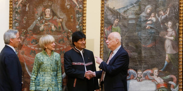 Backdropped by the paintings "Virgin of Candelaria," and "Escape to Egypt," Bolivia's President Evo Morales, second from right, shakes hands with Richard Huber, right, as Roberta Huber, second from left, and Bolivia's Vice President Alvaro Garcia, watch, during a ceremony recognizing the return of the stolen art, at the government palace, in La Paz, Bolivia, Thursday, April 9, 2015. Avid collectors, the Hubers returned the art work after learning from a museum that the two large paintings had been reported stolen from a Catholic church in southern Bolivia. (AP Photo/Juan Karita)