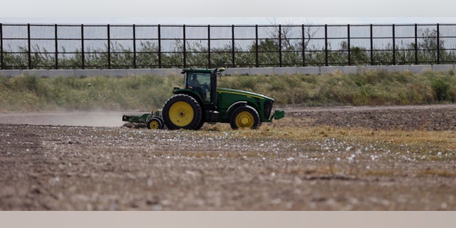 In this Sept. 6, 2012, photo, a tractor is used to farm in cotton field along a border fence that passes through the property in Brownsville, Texas. Since 2008, hundreds of landowners on the U.S.-Mexico border have sought fair prices for property that was condemned to make way for the fence, but many of them received initial offers that were far below market value. (AP Photo/Eric Gay)