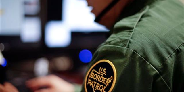 In this June 5, 2014, photo, a Border Patrol agent uses a headset and computer to conduct a long-distance interview by video with a person arrested crossing the border in Texas from a facility in San Diego.