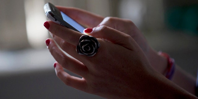 Aug. 21, 2013: A woman poses for a photo using her smartphone in Rio de Janeiro, Brazil. News reports say Google has removed a Brazilian Android application called "Rastreador de Namorados," or "Boyfriend Tracker" in Portuguese, from its Google Play app store, citing privacy concerns.