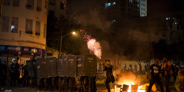 A police officer fires tear gas toward protesters during a march against bus fare hikes in Rio de Janeiro, Brazil, Friday, Jan. 8, 2016. The march, which is also taking place in other Brazilian capitals, began peacefully in downtown Rio de Janeiro but turned violent. (AP Photo/Felipe Dana)