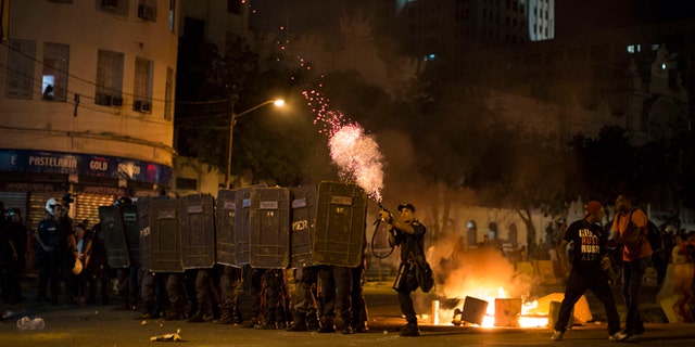 A police officer fires tear gas toward protesters during a march against bus fare hikes in Rio de Janeiro, Brazil, Friday, Jan. 8, 2016. The march, which is also taking place in other Brazilian capitals, began peacefully in downtown Rio de Janeiro but turned violent. (AP Photo/Felipe Dana)