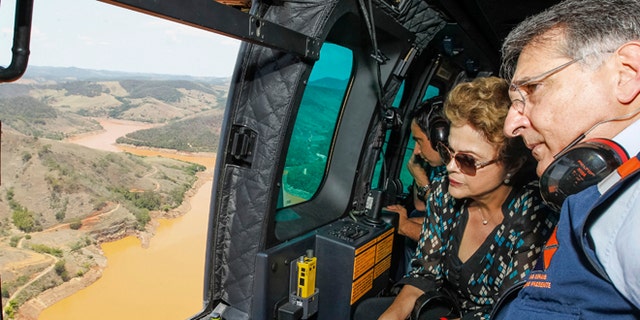 In this photo released by the official web site of the Brazilian Presidency, President Dilma Rousseff accompanied by Minas Gerais state Gov. Fernando Pimentel, looks out over the area of dam bursts at an iron ore mine, in the southeastern Brazilian state of Minas Gerais, Thursday, Nov. 12, 2015. Last week dam failures unleashed a deadly wave of viscous mud that all but erased a hamlet and contaminated a key river. Rousseff says the mining company, Samarco, will be made to pay for the cleanup. (Roberto Stuckert Filho/Brazil Presidential Press Office via AP)