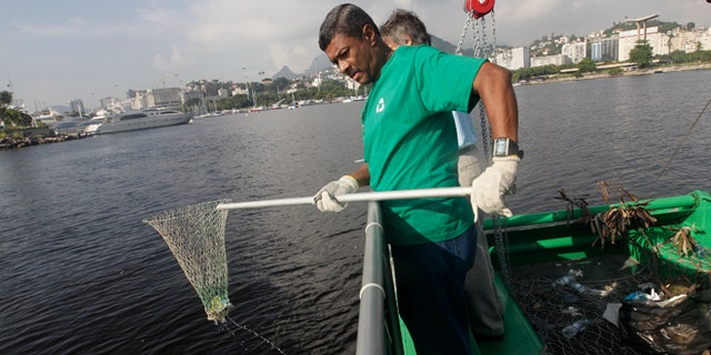 A worker fishes out trash from a garbage-collecting barge at the Guanabara bay, in Rio de Janeiro, Brazil, Monday, Jan. 6, 2014. The green barge plies the polluted waters of Rio de Janeiroâs Guanabara Bay alongside wooden fishing boats but its catch consists not of grouper or swordfish but rather plastic bags, empty soda bottles and a discarded toilet seat. The barge is one of three so-called "eco-boats," floating garbage vessels that are a key part of authorities' pledge to clean up Rioâs devastated Guanabara Bay before the city â and the waterway itself â plays host to the 2016 Olympic games. (AP Photo/Silvia Izquierdo)