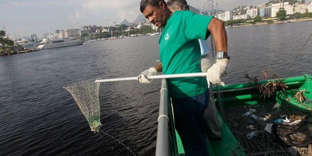 A worker fishes out trash from a garbage-collecting barge at the Guanabara bay, in Rio de Janeiro, Brazil, Monday, Jan. 6, 2014. The green barge plies the polluted waters of Rio de Janeiroâs Guanabara Bay alongside wooden fishing boats but its catch consists not of grouper or swordfish but rather plastic bags, empty soda bottles and a discarded toilet seat. The barge is one of three so-called "eco-boats," floating garbage vessels that are a key part of authorities' pledge to clean up Rioâs devastated Guanabara Bay before the city â and the waterway itself â plays host to the 2016 Olympic games. (AP Photo/Silvia Izquierdo)