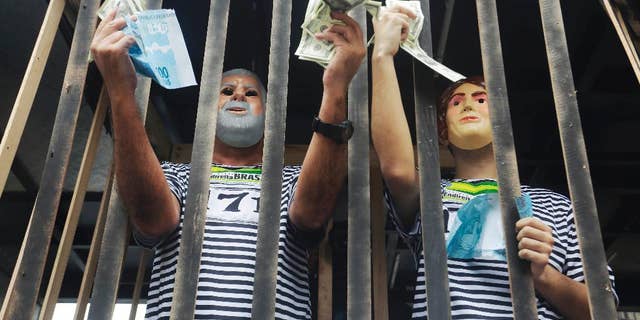 Demonstrators wearing masks depicting the former President Luiz Inacio Lula da Silva, left, and Brazil's President Dilma Rousseff holds fake money inside a mock jail during a protest march demanding the impeachment of Brazil's President Dilma, over an alleged scheme of corruption that siphoned money from the state-owned oil company Petrobras, in Sao Paulo, Brazil, Sunday, March 15, 2015. (AP Photo/Nelson Antoine)
