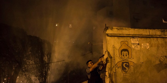 A Police officer of the Pacifying Police Unit, patrols among the smoke from burning barricades during clashes at the Pavao Pavaozinho slum in Rio de Janeiro, Brazil, Tuesday, April 22, 2014. Intense exchanges of gunfire, numerous blazes set alit and a shower of homemade explosives and glass bottles onto a busy avenue in Rio de Janeiros main tourist zone erupted Tuesday night after the death of a popular young shantytown resident. (AP Photo/Felipe Dana)