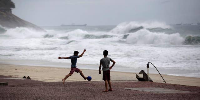 FILE - In this June 20, 2014 file photo, boys play football as waves break on Sao Conrado beach in Rio de Janeiro, Brazil. World Surf League spokesman Dave Prodan said in an emailed statement Wednesday, April 29, 2015, that Sao Conrado beach had to be removed from its venue list “due to pollution issues.” The beach had been a backup for the May 11-22 Rio Pro event, to be used in case of sub-par waves or other issues at the primary venue, nearby Barra da Tijuca beach. (AP Photo/Matt Dunham, File)