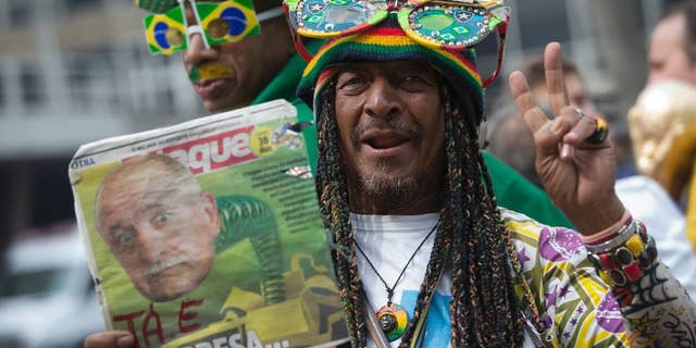 A Brazil soccer fan holds up a newspaper with a photo of Brazil's coach Luiz Felipe Scolari and flashes a victory sign outside the venue where coach Luiz Felipe Scolari is announcing his squad for the upcoming international soccer tournament in Rio de Janeiro, Brazil, Wednesday, May 7, 2014. The team will mix talented young stars such as Neymar and Oscar with more experienced players such as Dani Alves, David Luiz, Thiago Silva and Hulk. Past stars such as Ronaldinho, Kaka and Robinho were left off the squad as expected. (AP Photo/Silvia Izquierdo)