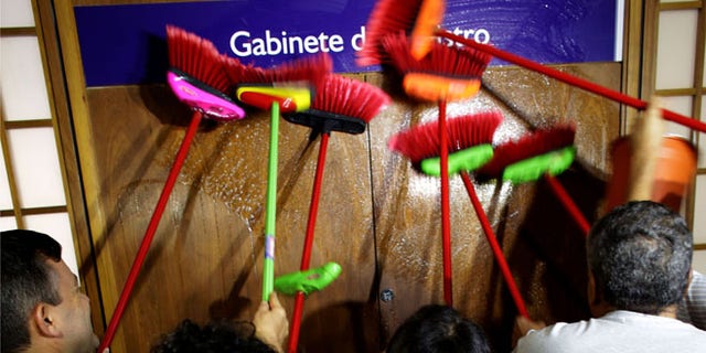 Ministerial staff use brooms to scrub the office door of the Transparency Minister Fabiano Silveira demanding his resignation, in Brasilia, Brazil, Monday, May 30, 2016. A recording TV Globo broadcast late Sunday shows Silveira criticizing Operation Car Wash, a wide-ranging corruption probe of the state oil company Petrobras that has implicated numerous leading Brazilian politicians and businessmen. Protesters in Brazil use brooms as a representation to sweep away corruption. (AP Photo/Eraldo Peres)