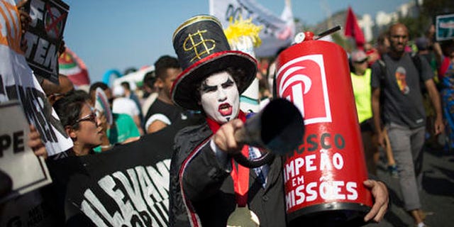 A demonstrator in a costume depicting a banker and holding a replica of a fire extinguisher for putting out the "flame" of an imitation Olympic torch, takes part in a protest against the interim Brazilian president Michel Temer, and the Rio's 2016 Summer Olympics, on the route of the Olympic torch, at the Copacabana beach, in Rio de Janeiro, Brazil, Friday, Aug. 5, 2016. (AP Photo/Leo Correa)
