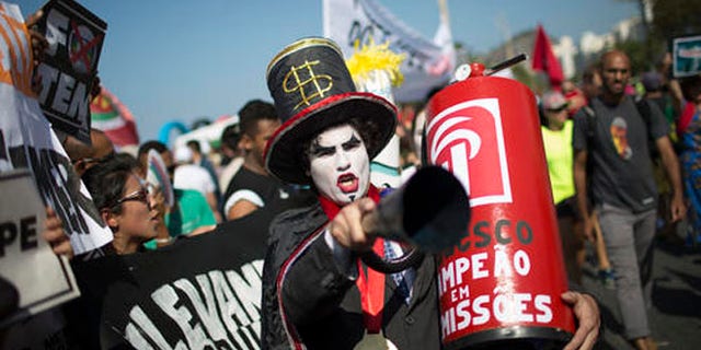 A demonstrator in a costume depicting a banker and holding a replica of a fire extinguisher for putting out the "flame" of an imitation Olympic torch, takes part in a protest against the interim Brazilian president Michel Temer, and the Rio's 2016 Summer Olympics, on the route of the Olympic torch, at the Copacabana beach, in Rio de Janeiro, Brazil, Friday, Aug. 5, 2016. (AP Photo/Leo Correa)