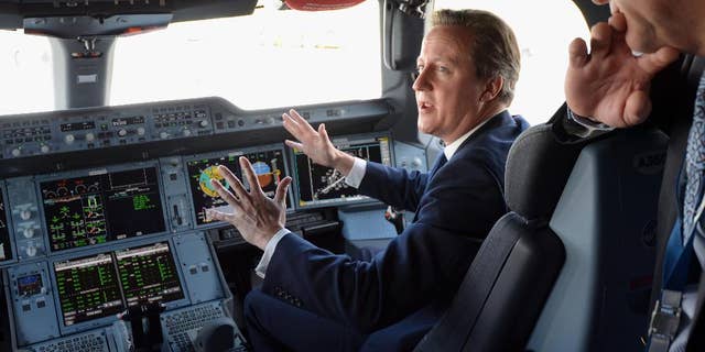 Britain's Prime Minister David Cameron, background, sits in the co-pilots seat, in the cockpit as he is shown around an Airbus A350, during a visit to the 2014 Farnborough Airshow in Hampshire, England, Monday July 14, 2014. (AP Photo/Andrew Matthews, Pool)