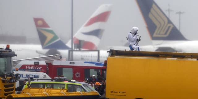 Emergency service workers talk to an activist, dressed as a teddy bear, top right, from the pressure group Plane Stupid, who was one of several demonstrators who occupied the north runway at London's Heathrow Airport to launch a protest Monday July 13, 2015. A spokesman for the action group said a dozen demonstrators cut through a fence and entered the runway early on Monday. (Steve Parsons/PA via AP) UNITED KINGDOM OUT