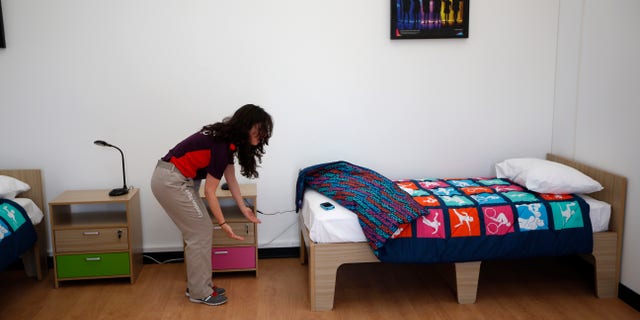 July 12, 2012: An Olympic volunteer shows with her hands an approximation of how much further the length of a standard bed could be extended in length for taller athletes in a display bedroom, that was larger that the real room athletes will have, during a media opportunity at the Olympic and Paralympic athlete's village in London.
