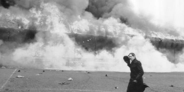 FILE - In this May 11, 1985 file photo, a police officer runs past the blazing main stand at Bradford City's Valley Parade football ground in Bradford, England. It’s approaching 30 years since Valley Parade, Bradford’s home ground, became an inferno. Fifty-six spectators died and 265 were injured when a fire broke out and engulfed a wooden main stand holding about 3,500 fans during the team’s final match of the season against Lincoln. (PA via AP, File) UNITED KINGDOM OUT, NO SALES, NO ARCHIVE