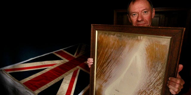 Sept. 20, 2010: Adrian Raeside from Canada, holds a photograph of his grandfather Sir Charles Seymour Wright and great-uncle Thomas Griffith Taylor in front of a silk union flag that belonged to captain Robert Falcon Scott and was used on the two expeditions he led to the Antarctic at the Christie's auction house in London.