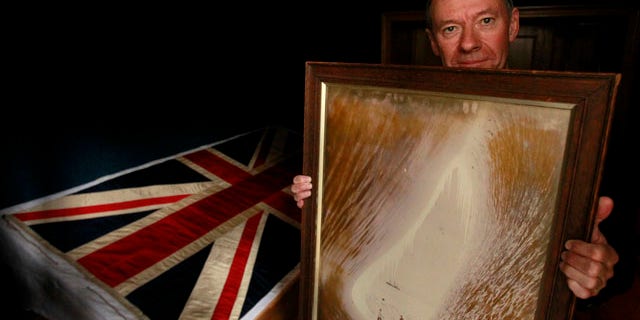 Sept. 20, 2010: Adrian Raeside from Canada, holds a photograph of his grandfather Sir Charles Seymour Wright and great-uncle Thomas Griffith Taylor in front of a silk union flag that belonged to captain Robert Falcon Scott and was used on the two expeditions he led to the Antarctic at the Christie's auction house in London.