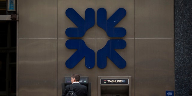 June 13, 2013: A man stands under a RBS, Royal Bank of Scotland, logo as he uses an ATM outside a branch of the bank in London.