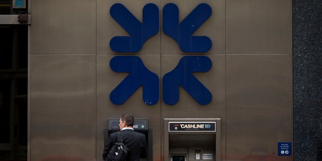 June 13, 2013: A man stands under a RBS, Royal Bank of Scotland, logo as he uses an ATM outside a branch of the bank in London.