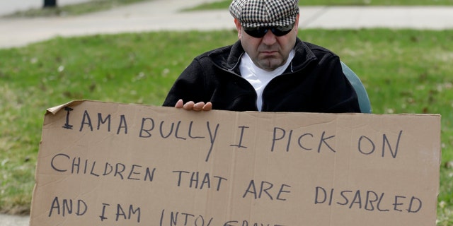 Following court orders, Edmond Aviv sits on a street corner holding a sign Sunday, April 13, 2014, in South Euclid, Ohio.