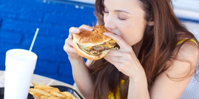 Beautiful young lady eating a tasty burger at an outdoor cafe. Horizontal Shot.