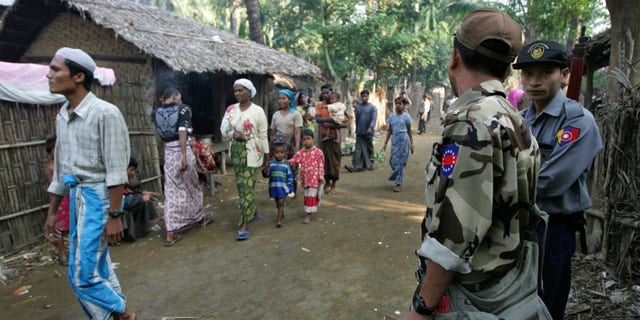 Nov. 10, 2012: In this photo, Muslim refugees walk as Burma police officers stand guard at Sin Thet Maw relief camp in Pauktaw township, Rakhine state, western Burma.