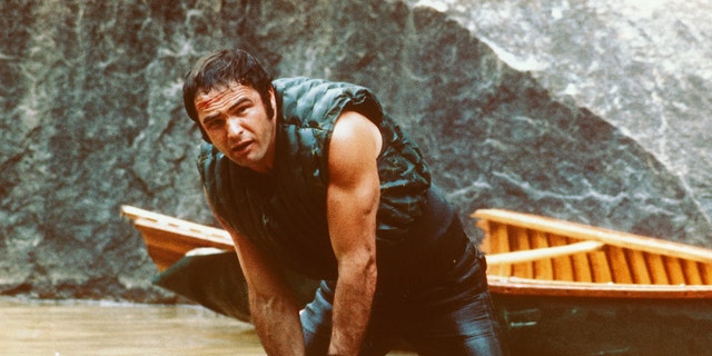 Burt Reynolds, US actor, holding onto some rocks as he struggles in the water with his boat behind him in a publicity still issued for the film, 'Deliverance', USA. The 1972 thriller, directed by John Boorman, starred Reynolds as Lewis Medlock. 