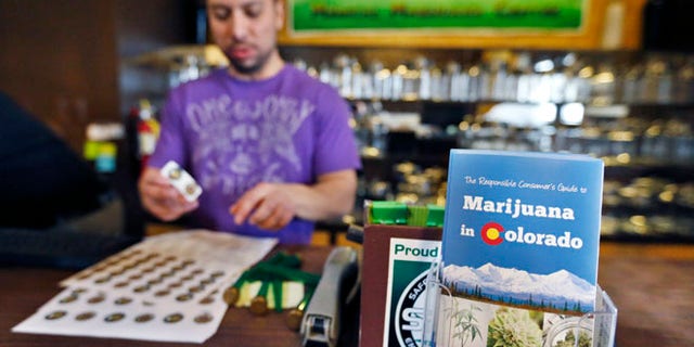 General manager David Martinez labels containers of retail marijuana, behind a sales bar fitted with a brochure available to customers, at 3D Cannabis Center in Denver, Dec. 31, 2013.