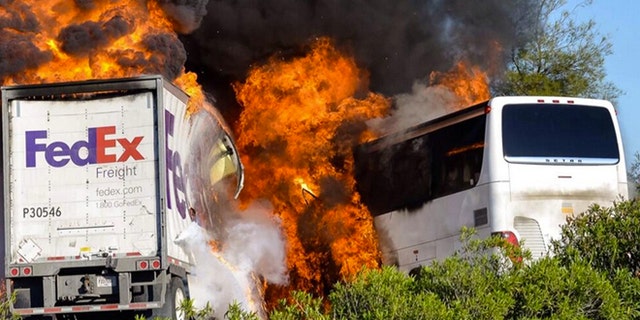 Massive flames are seen devouring both vehicles just after the crash, and clouds of smoke billowed into the sky Thursday April 10, 2014 until firefighters had quenched the fire, leaving behind scorched black hulks of metal. The FedEx tractor-trailer crossed a grassy freeway median in Northern California and slammed into the bus carrying high school students on a visit to a college. At least nine were killed in the fiery crash, authorities said. (AP Photo/Jeremy Lockett)