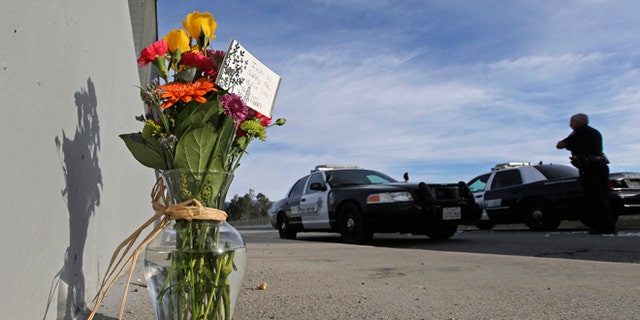 FILE - In this Dec. 3, 2015 file photo, flowers are left by the side of the road as a San Bernardino police officer blocks the road leading to the site of yesterday's mass shooting in San Bernardino, Calif.  President Barack Obama plans to meet with families of victims of the mass shooting in San Bernardino, California, the White House said Wednesday. The meeting is set for Friday. Obama is adding the stop in Southern California to a long-scheduled trip to Hawaii for Christmas vacation. (AP Photo/Chris Carlson, File)