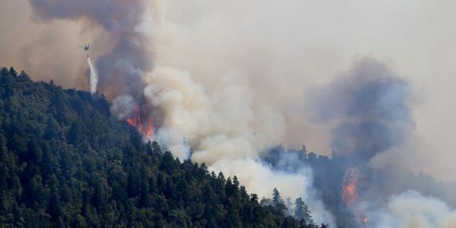 August 8, 2014: An Air National Guard helicopter makes a water drop as the Lodge Fire between Legget tand Laytonville, Calif., jumps the Eel River and moves upslope. (AP/Kent Porter)