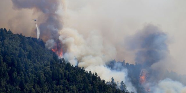 August 8, 2014: An Air National Guard helicopter makes a water drop as the Lodge Fire between Legget tand Laytonville, Calif., jumps the Eel River and moves upslope. (AP/Kent Porter)