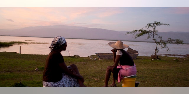 In this Aug. 22, 2013 photo, vendors Jacline Bienheme, left, and Marie Jolerme wait for fishermen to return on the shores of Lake Azuei in Thomazeau, Haiti. Experts are sounding a new alarm about the effects of climate change for parts of the Caribbean: the depletion of already strained drinking water throughout much of the region. (AP Photo/Dieu Nalio Chery)