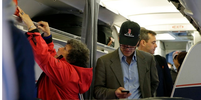 FILE - In this Thursday, Oct. 31, 2013 file photo, a passenger checks his cell phone while boarding a flight, in Boston. Allowing airline passengers to make cellphone calls in-flight is asking for trouble, lawmakers said Tuesday, Feb. 11, 2014, as a House panel approved a bill to ban such calls. (AP Photo/Matt Slocum)