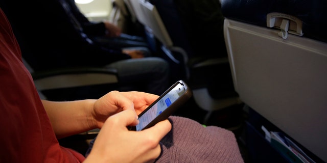 FILE - This Oct. 31, 2013 file photo shows a plane passenger checking her cell phone before a flight in Boston. While one government agency considers allowing cellphone calls on passenger planes, another now wants to ban them. The Transportation Department signals that it wants to impose a ban on inflight cellphone calls, just two months after the Federal Communications Commission (FCC) voted to pursue lifting the current ban. The FCC regulates wireless communications, while the transportation department regulates issues affecting airline passengers. (AP Photo/Matt Slocum, File)