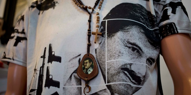 A T-shirt of fugitive Mexican drug lord Joaquin "El Chapo" Guzman covers a mannequin representing Jesus Malverde, known in Mexico as the "Saint" of drug traffickers, inside the shrine of a faith healer in Mexico City, Friday, Oct. 16, 2015. The government is offering a reward of 60 million pesos, or about $3.5 million dollars, for Guzman's recapture after he made his second escape from a maximum security prison through an underground tunnel in 2015. (AP Photo/Eduardo Verdugo)