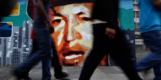 People walk by a mural of Venezuela's President Hugo Chavez in Caracas, Venezuela, Friday, April 20, 2012. Chavez is in Cuba to continue with cancer treatment. (AP Photo/Ariana Cubillos)